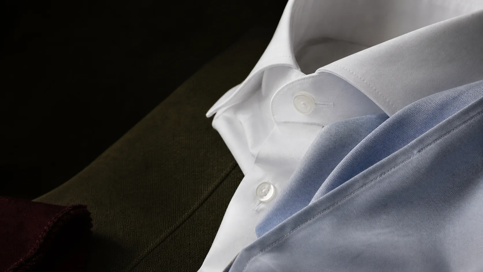 Close detail of premium shirting fabric, collar stitching and mother-of-pearl buttons.